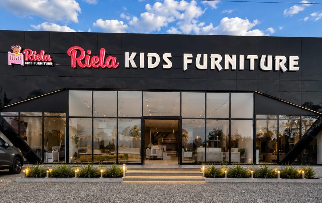 The Riela Kids Furniture showroom at dusk with glass frontage and lit displays inside